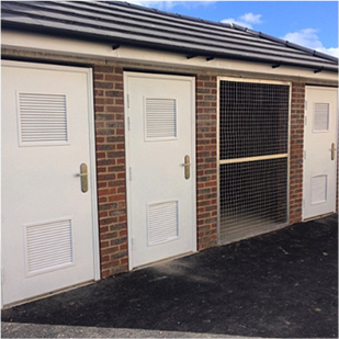 Three white doors on a brick building with a steel cage separated one of the doors from the other two